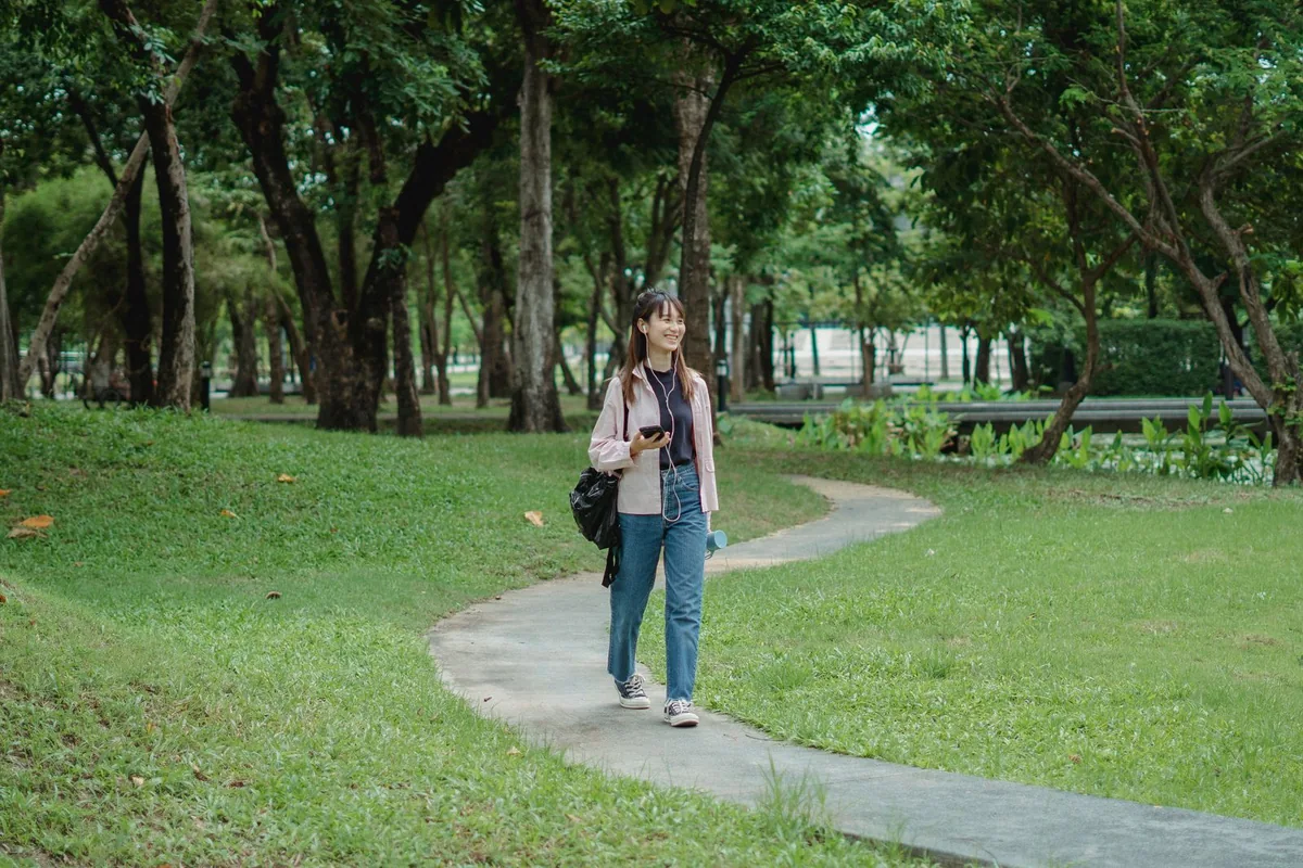 Woman listening with earphones while walking through a green park.