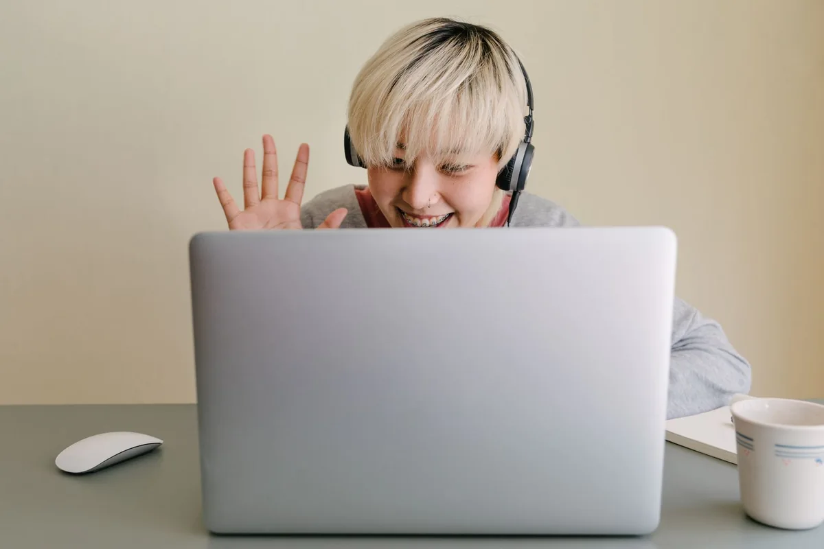 Woman wearing headphones and waving during a laptop video call.