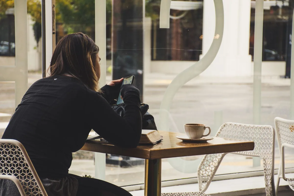 Woman using her phone beside a cup of coffee in a cafe.