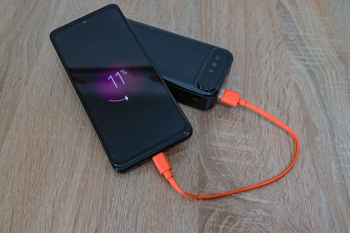 Phone connected to a power bank with an orange cable on a wooden table.