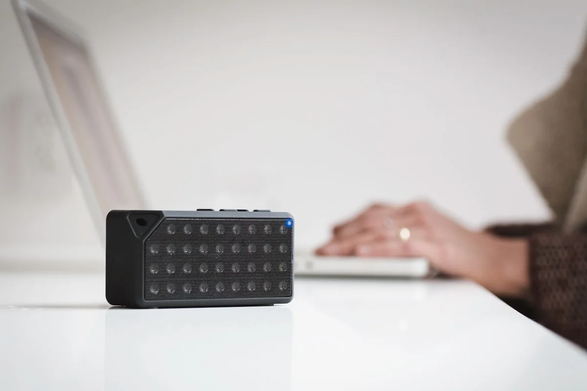 Compact wireless speaker on a desk beside a laptop.