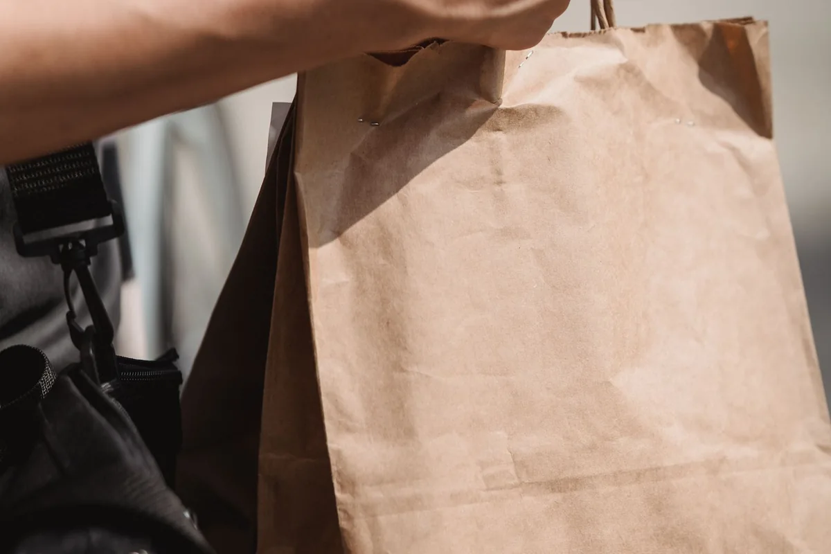 Shopper holding a phone and paper shopping bags outdoors.