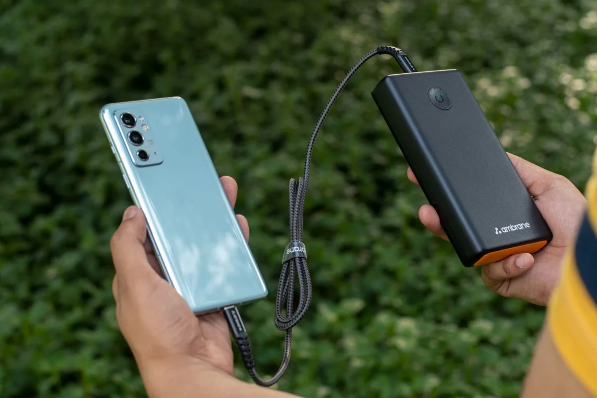 Hands holding a phone connected to a portable charger outdoors.